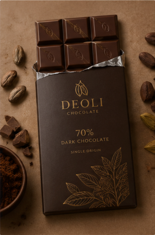 A bar of DEOLI 70% dark chocolate in its wrapper, styled on a textured brown background with scattered cocoa beans, chocolate pieces, and a small bowl of cocoa powder.